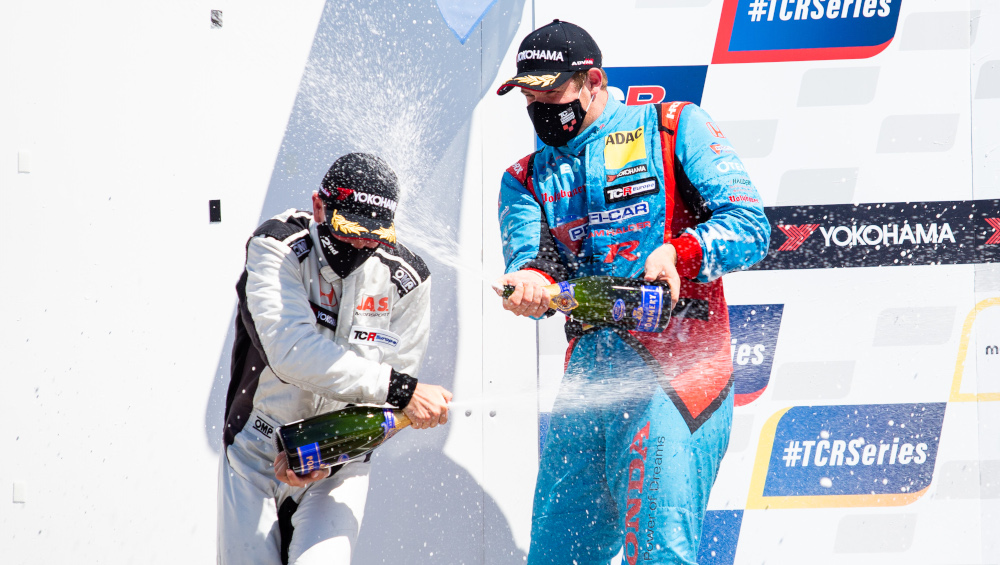 Mike Halder celebrates on the podium by spraying champagne whilst wearing a mask